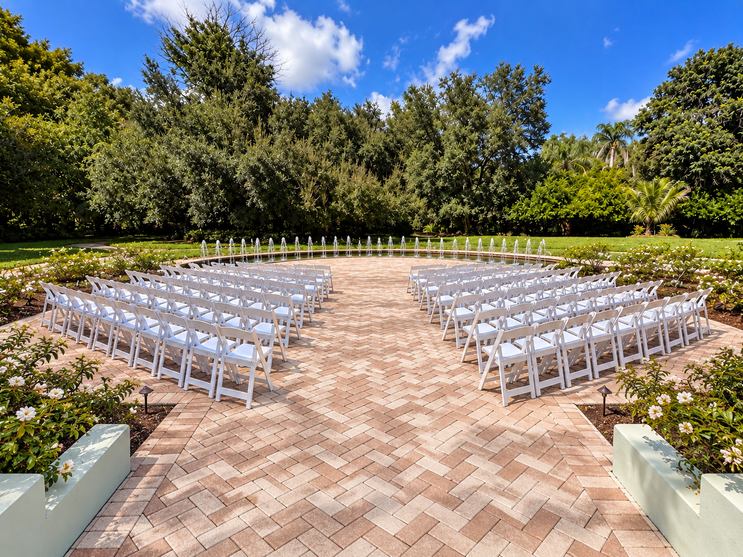 Photo of the Rose Garden wedding site. It features a small fountain, green trees, and rows of white chairs.