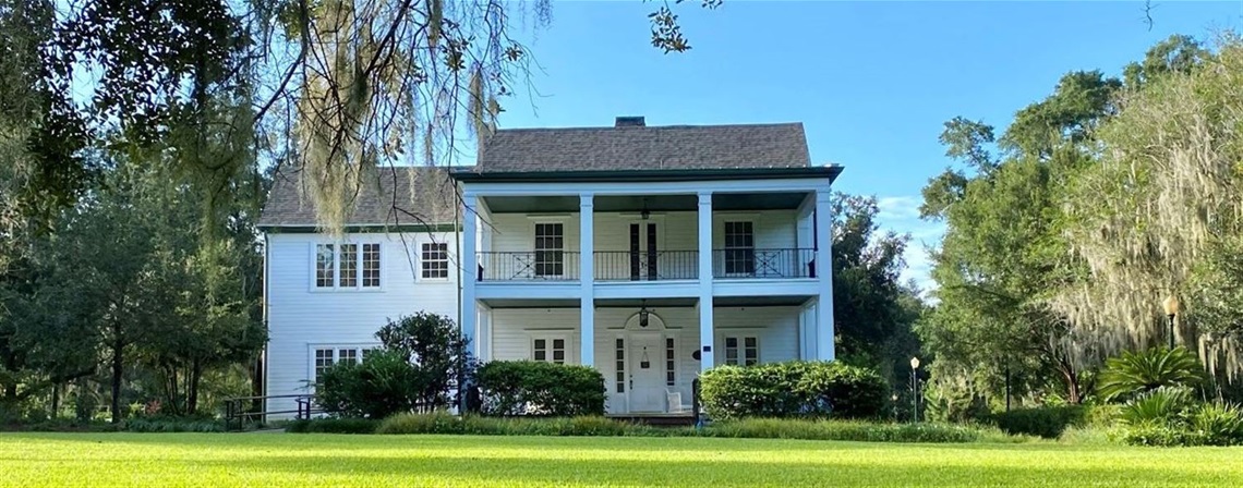 A white two story house surrounded by a green lawn and trees