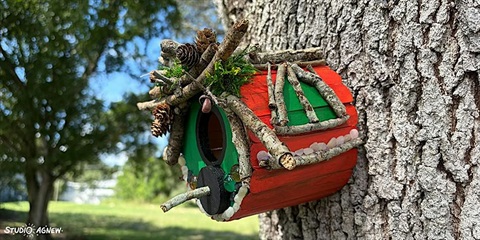 Red birdhouse with green elements, attached to a tree.