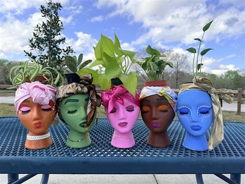 Plants in pots that look like colorful heads. The plants are green and leafy.