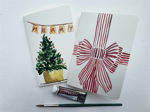 White cards painted in watercolor, featuring a green Christmas tree and pink bow.