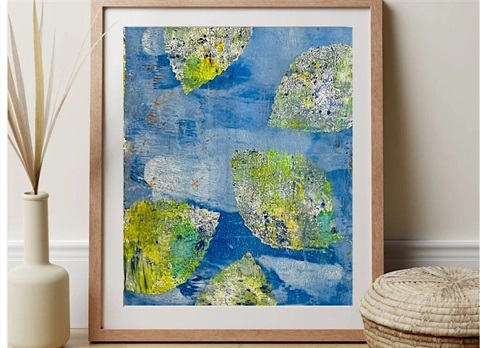 A framed gel plate print of green leaves on a blue background