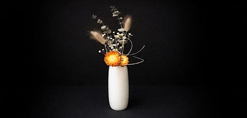 A miniature dried Ikebana Japanese floral arrangement in a white vase