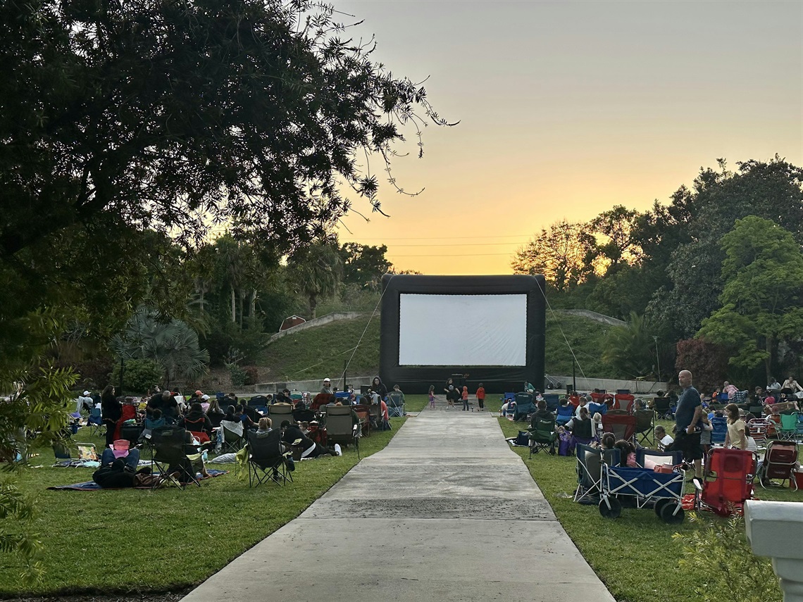 Attendees in lawn chairs watching a movie on a large screen in the garden