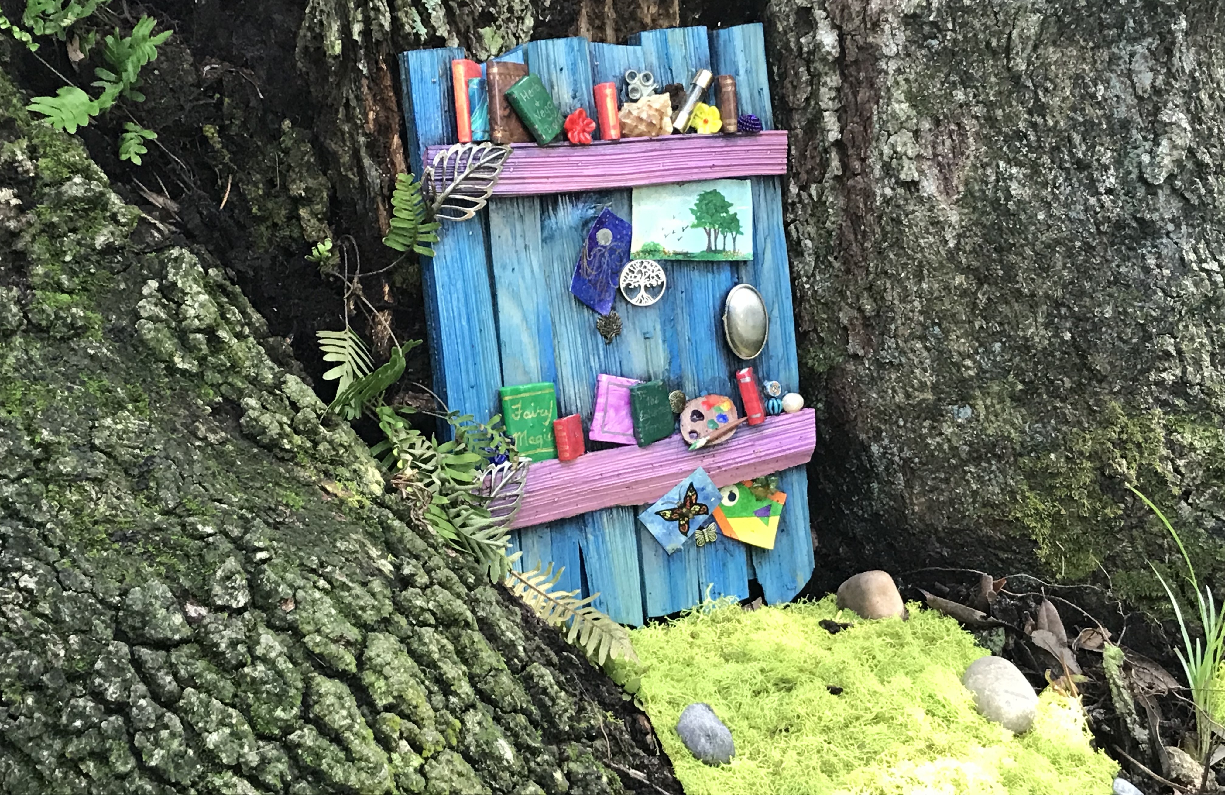 Blue fairy door next to a tree trunk.